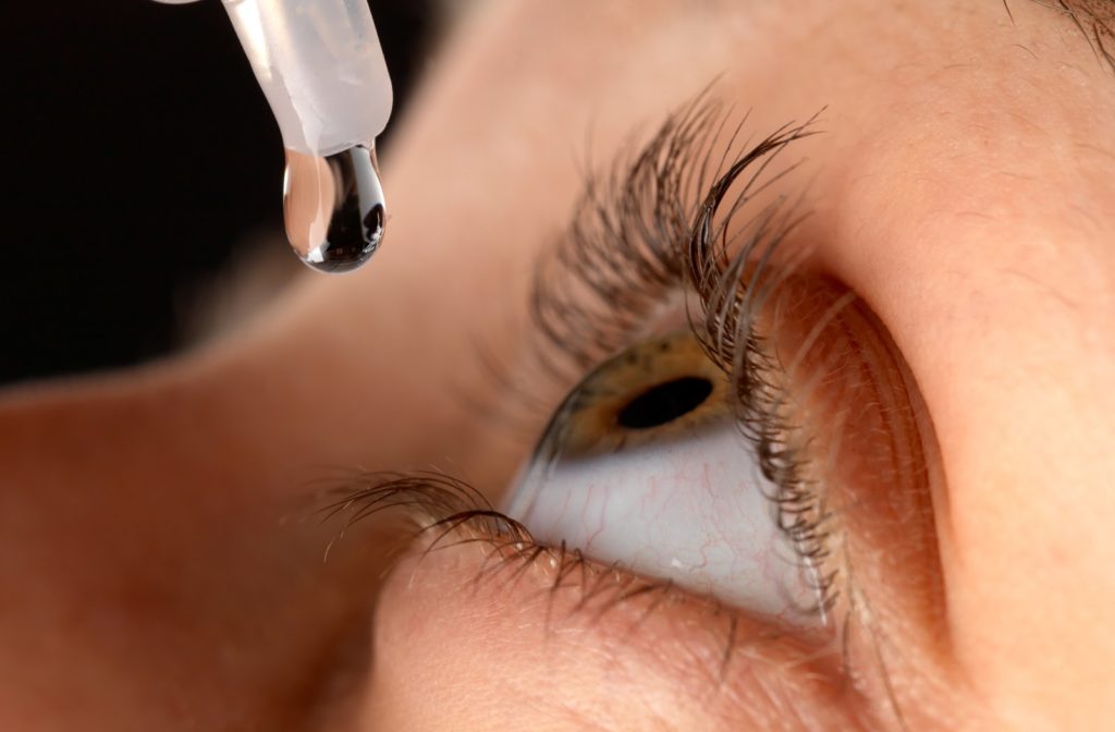close up of woman with green eyes putting eye drops in to her eye