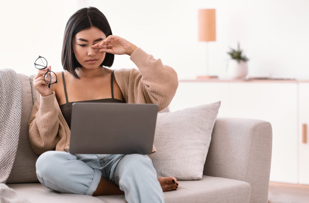 Women experiencing red and itchy eyes due to too much screen time using laptop in living room of house