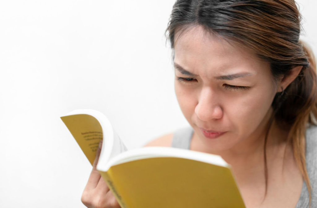 A lady is reading a yellow book with her face so near to what she is reading.