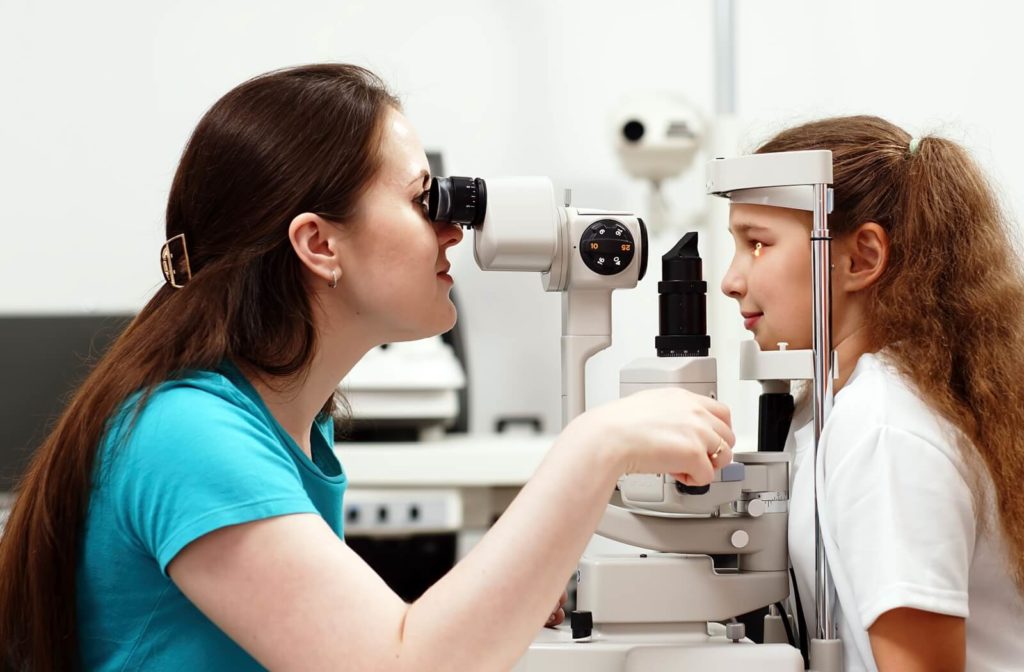 Optometrist performing a routine eye exam on a young child with a slit lamp in a clinical setting