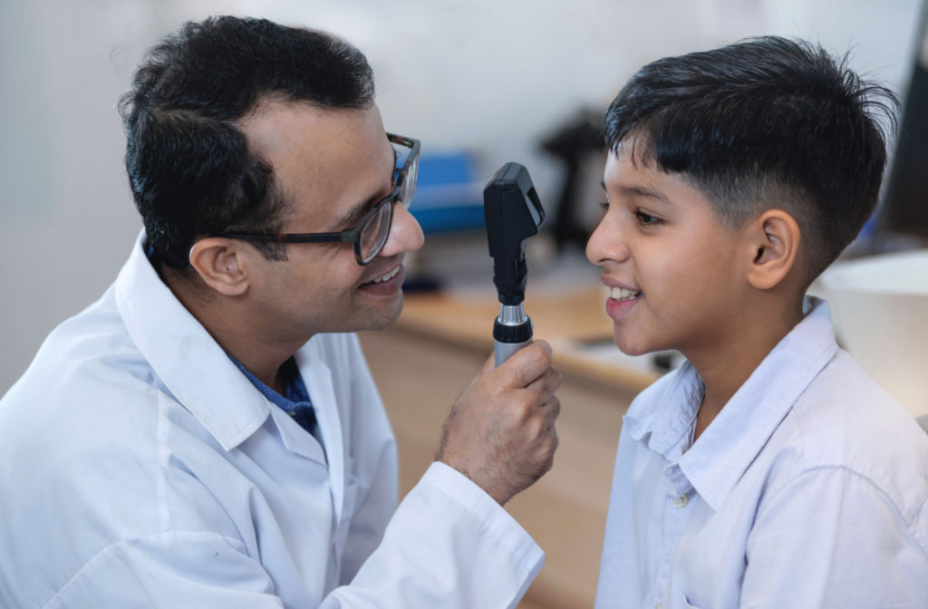 An eye doctor smiling and using a retinoscope to look at a child's right eye.