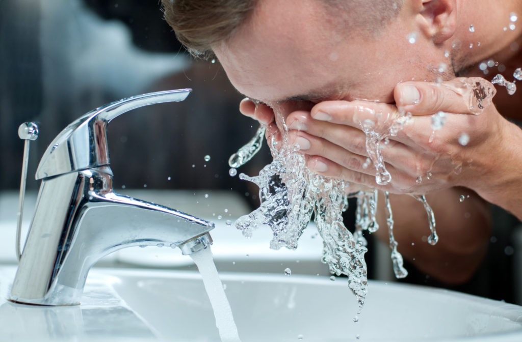A man washing his face in the sink with water.