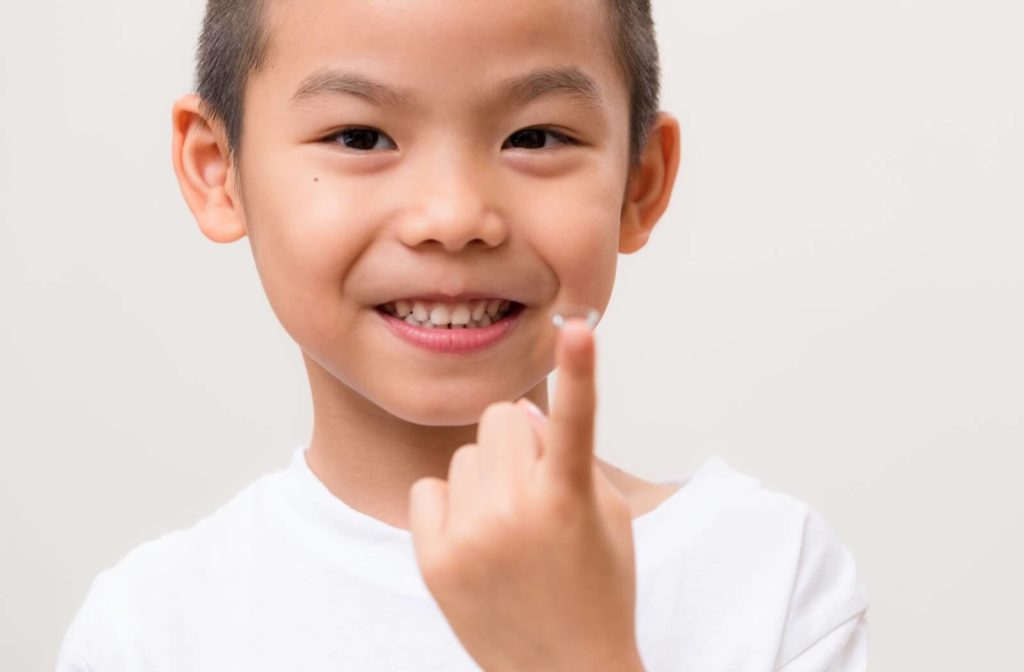 A child smiling and holding a contact lens on one index finger.