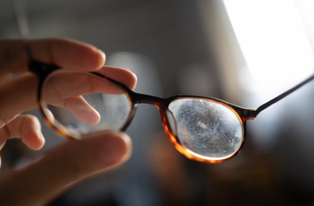 A close-up image of a pair of scratched glasses in front of of a window.