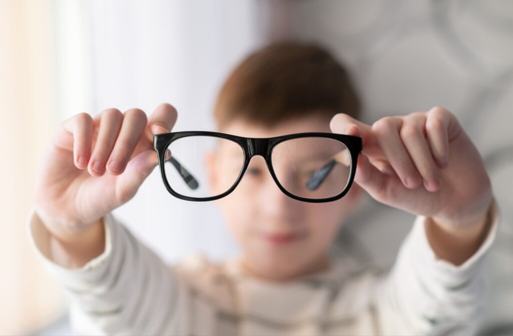 Child holding out glasses with blurred surroundings, symbolizing myopia and the importance of early management to slow its progression.