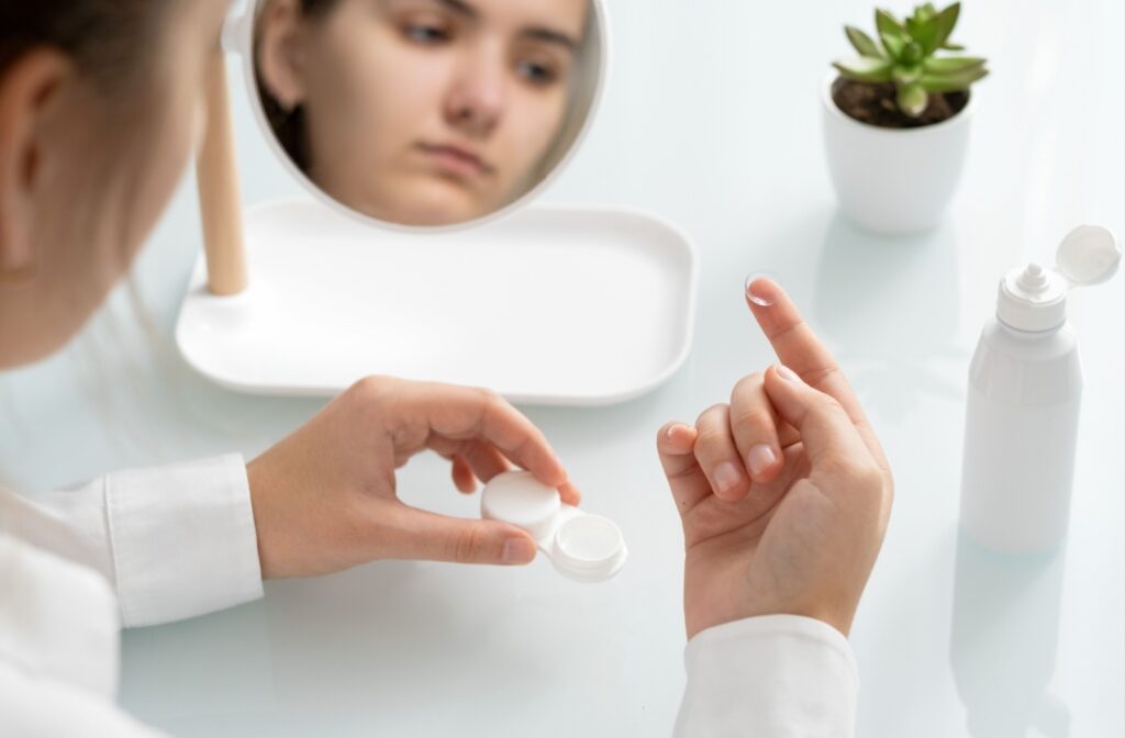 A person holding a contact lens in their hand above a table that has a bottle of contact solution.