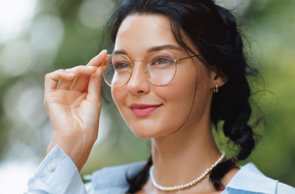 A young adult looks into the distance while resting a hand on the thing metal framed glasses she is wearing