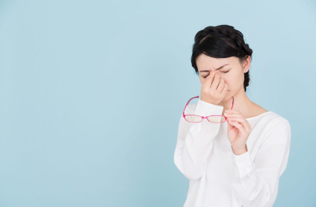 A person holding their glasses while they pinch in between their eyes to attempt to relieve eye strain